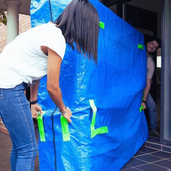 Mattress cover for moving being used by two people to carry a heavy mattress through the doorway of a new home, using the handles