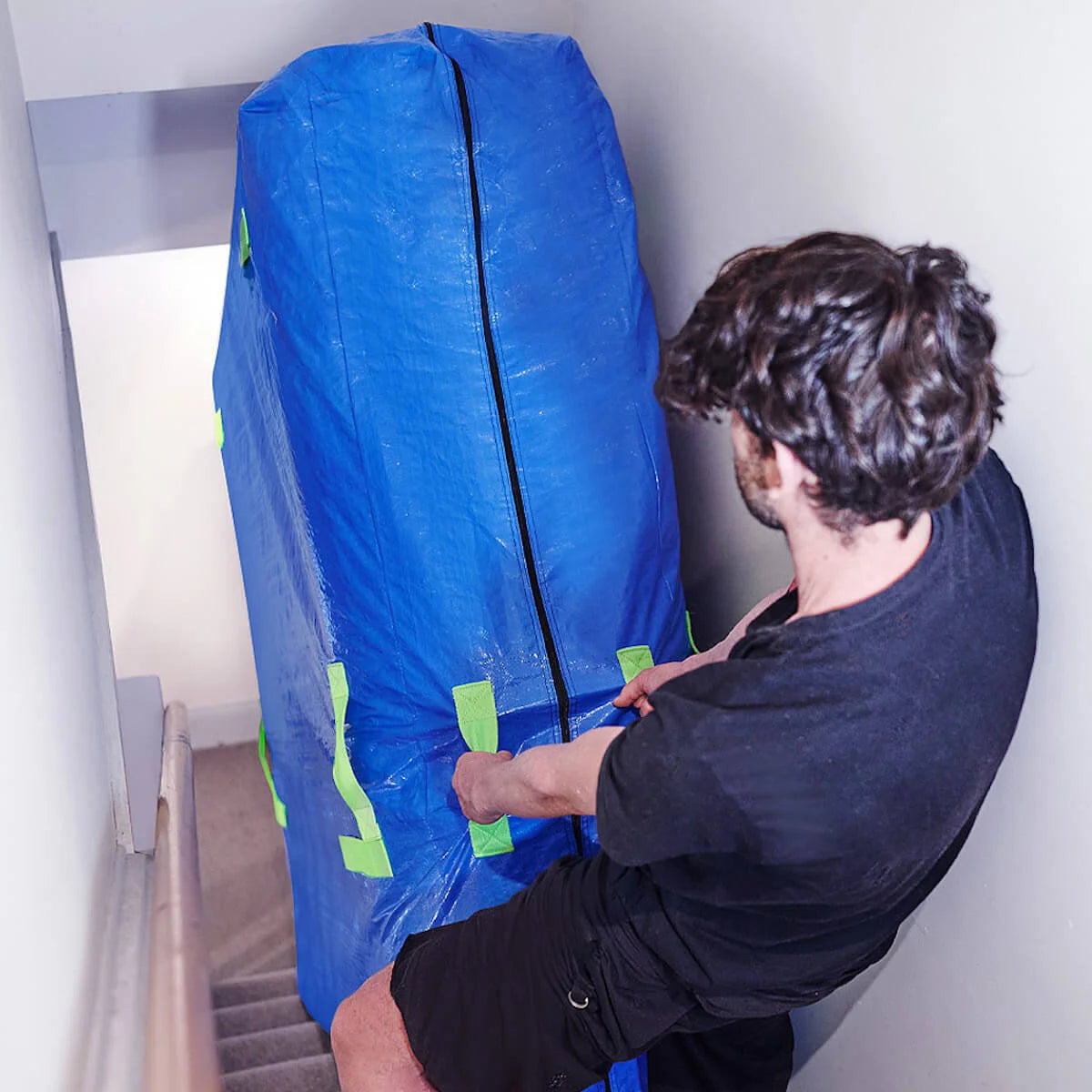 Mattress bag for moving being dragged upstairs by a man using the end handles for easy transporting before it goes into storage