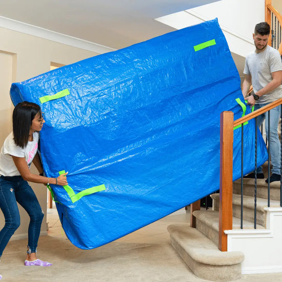 Two people transporting the mattress upstairs in a heavy-duty mattress cover for moving with many handles